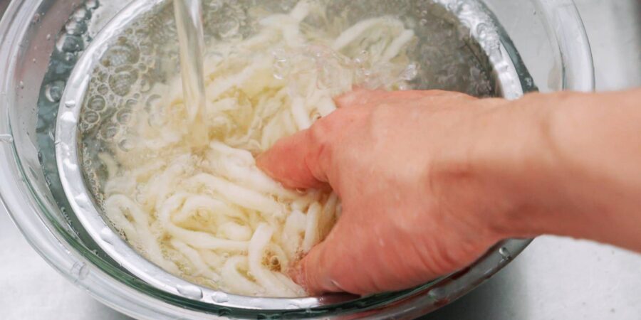 Washing udon noodles to remove extra starch.