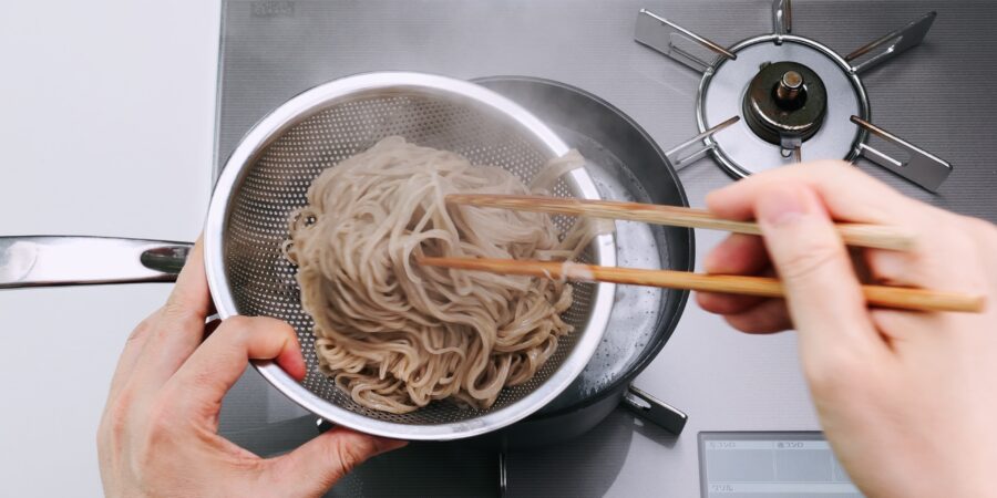 Transferring the cooked soba from the pot to a strainer.
