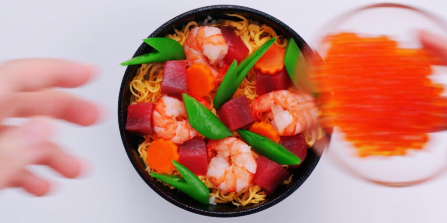 Chirashi sushi bowl topped with tuna, shrimp, eggs, carrots and snap peas.