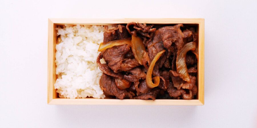 Packing Gyunabe on rice in a wooden bento box.