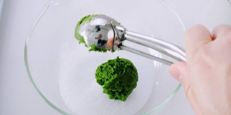 Scooping matcha cookie dough into sugar.