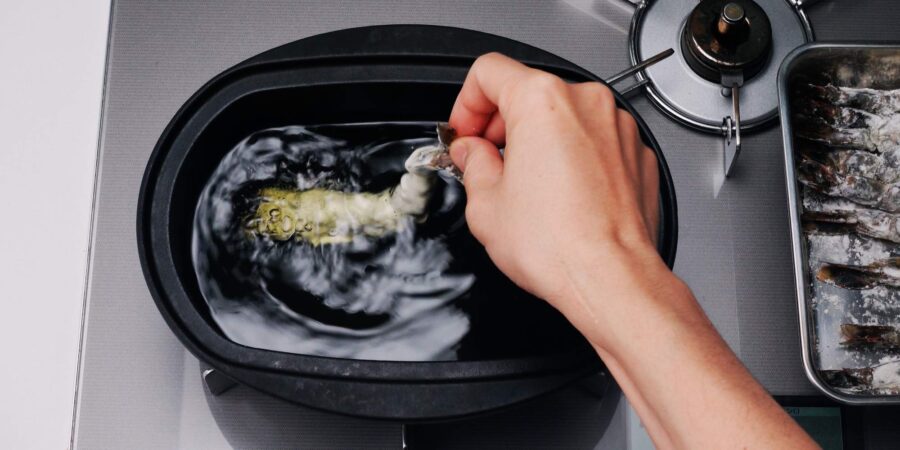 Adding battered shrimp to oil.
