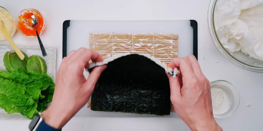 Flipping nori and rice over on a sushi mat to make an inside out sushi roll.