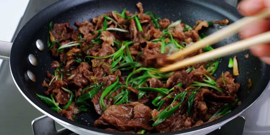 Cooked beef with green onions in a frying pan.