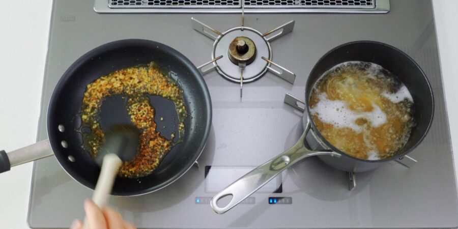 Browning soy sauce in frying pan while pasta boils on the other burner.