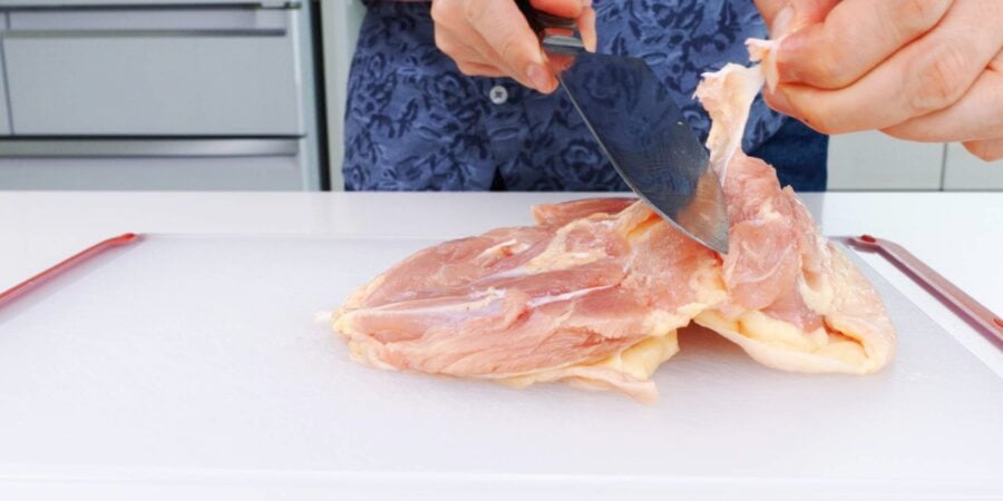 Trimming excess fat and connective tissue from chicken thighs.