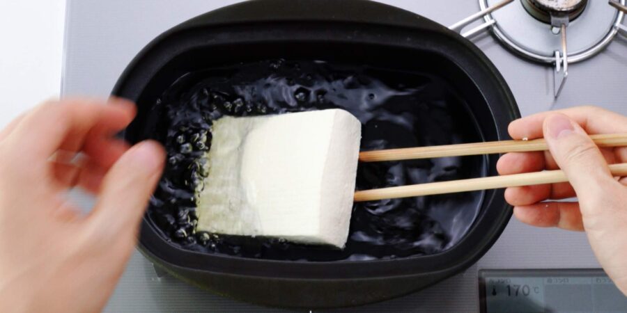 Lowering tofu into frying oil to make atsuage.