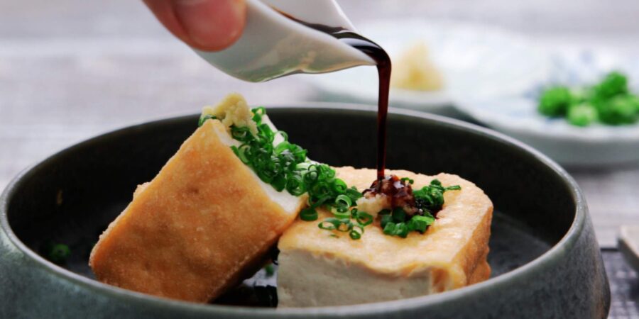 Pouring soy sauce onto Atsuage with scallions and ginger.