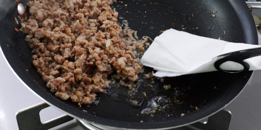 Draining excess fat from ground pork with a paper towel.