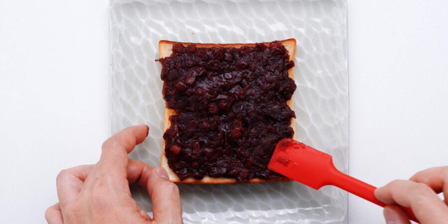 Spreading anko onto buttered toast with a spatula.