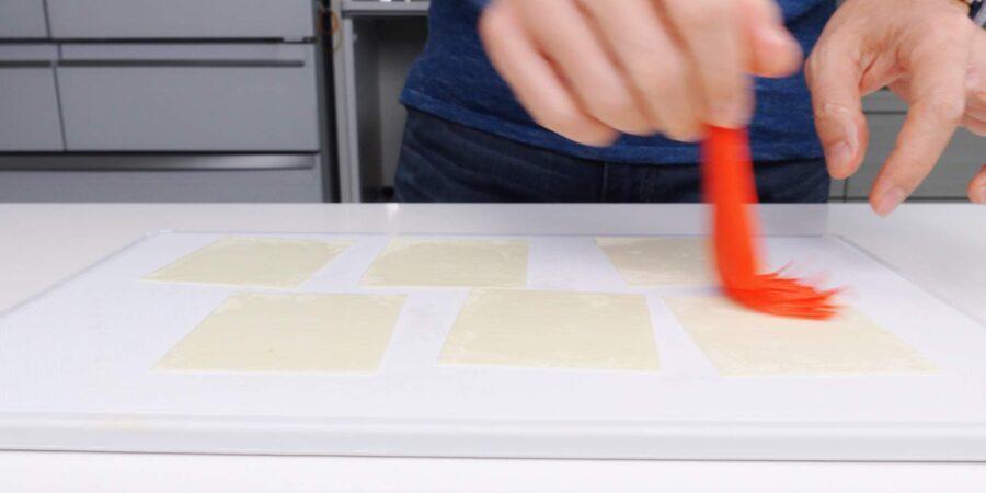 Brushing sesame oil onto wonton wrappers with a red pastry brush.