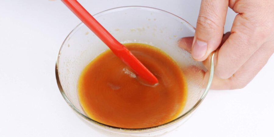 Whisking Chinese Chicken Salad dressing together in a glass bowl with a small spatula.