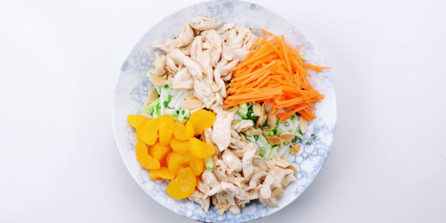 Mandarins and julienned carrots along with shredded chicken on an Asian chicken salad.