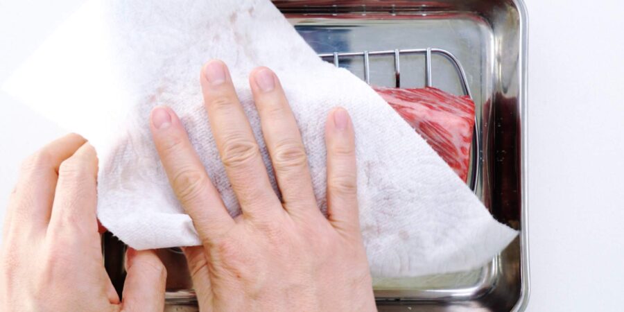 Patting wagyu beef dry with paper towels.