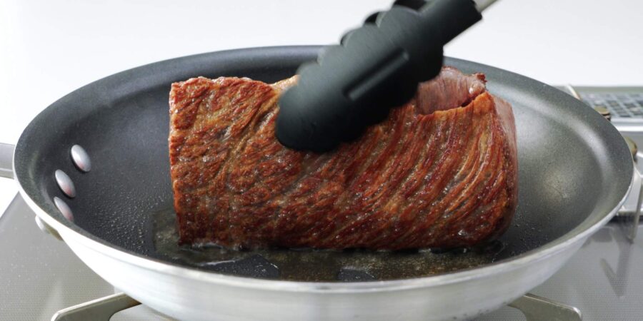 Browned wagyu beef sizzling in a pan.