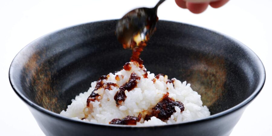 Drizzling onion sauce onto a bowl of rice.