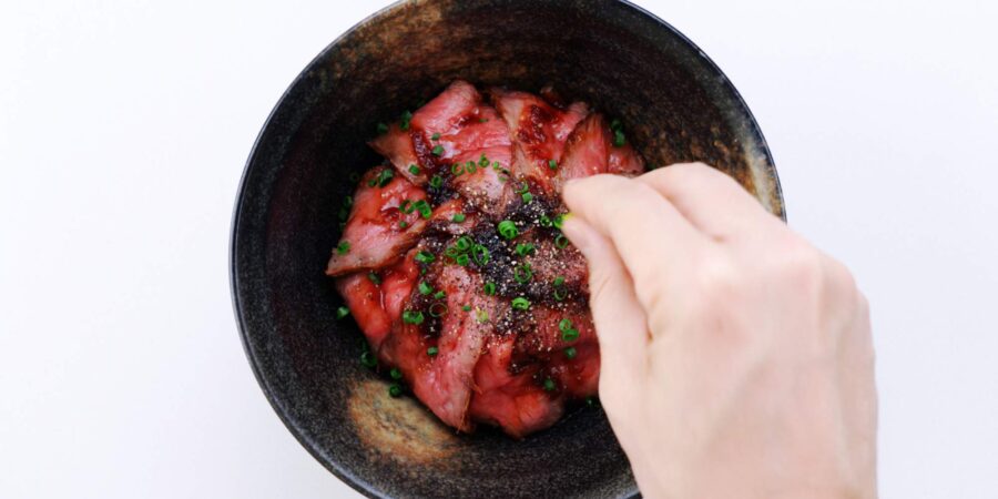 Roast beef rice bowl garnished with black pepper and scallions.