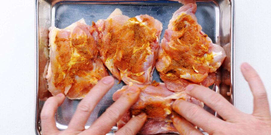 Spreading garlic curry paste onto chicken thighs.