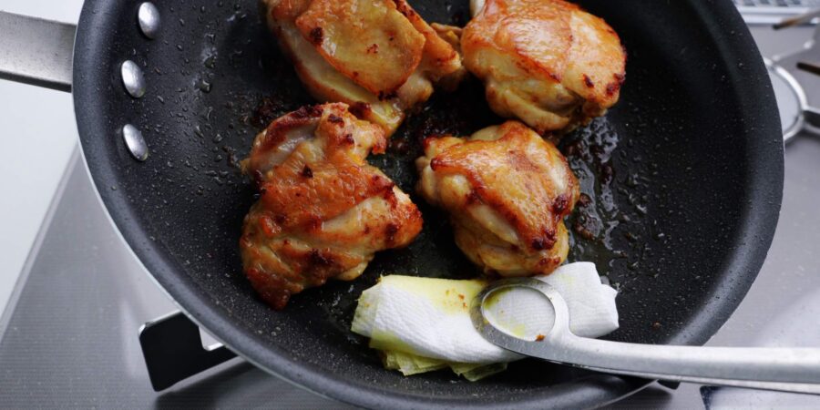 Draining excess oil from a frying pan with chicken.