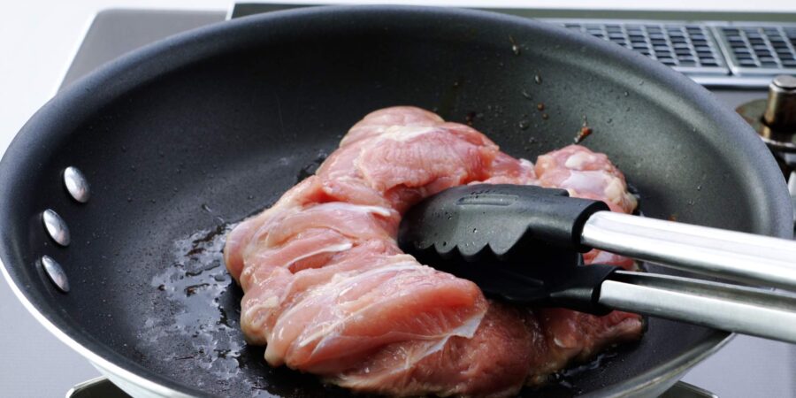 Pan-frying skin-side of chicken while pressing down on it with tongs.