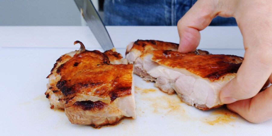 Slicing pan-roasted chicken in half after resting for 10 minutes.