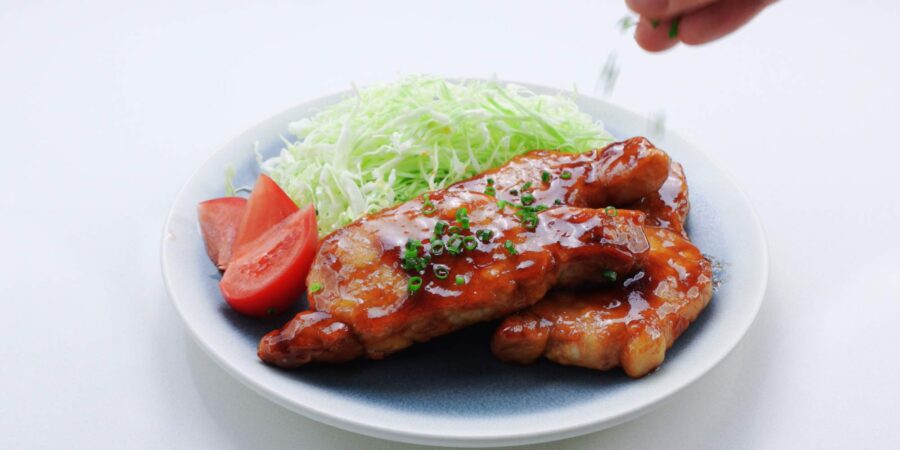 Sprinkling chopped green onions on a plate of Japanese ginger pork.