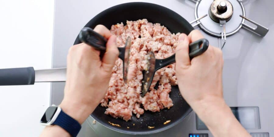 Chopping up ground chicken with two spatulas.
