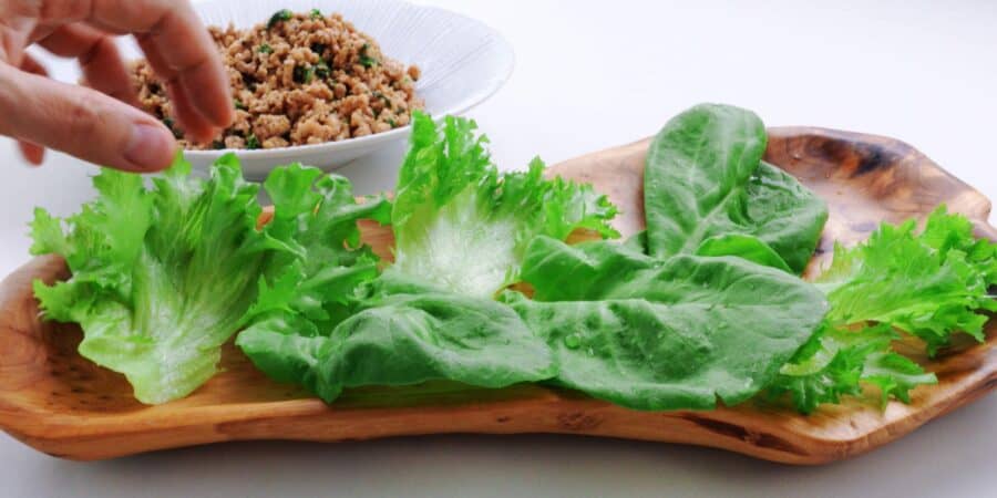 Lettuce leaves lined up on a wooden platter with basil chicken stir-fry in the background.