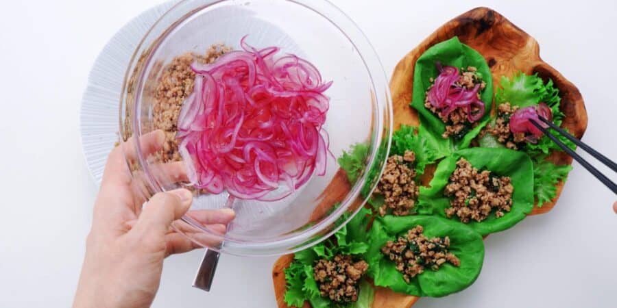 Bowl of lime pickled red onions with chicken lettuce wraps below.