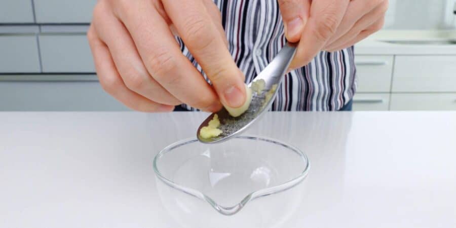 Grating garlic into a small glass bowl.