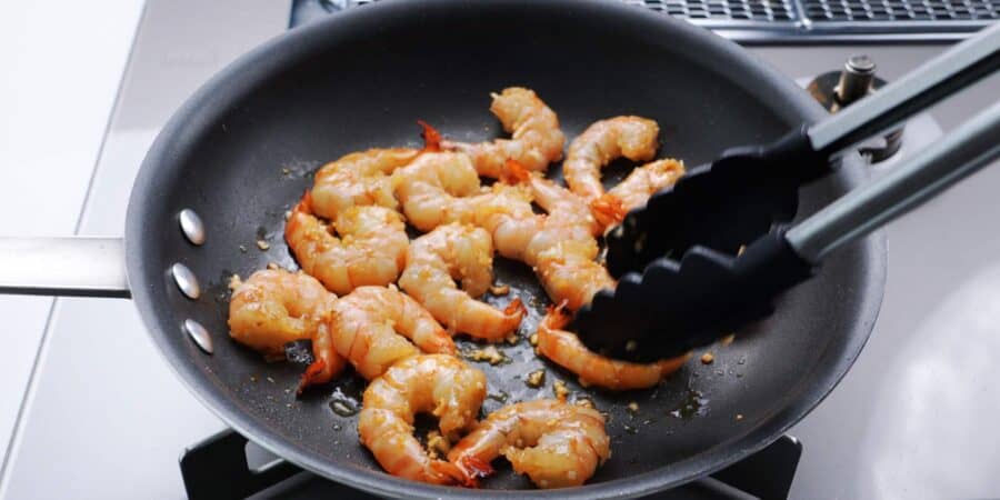 Flipping shrimp over in a frying pan.