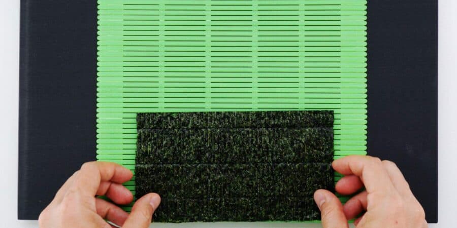 Half sheet of nori placed on the bottom edge of a sushi mat.