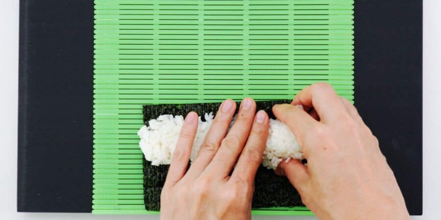 Pressing sushi rice across a sheet of nori.