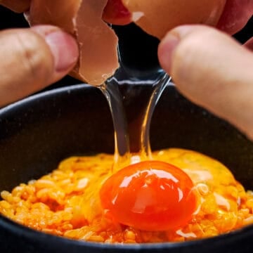 Breaking a raw egg over a bowl of golden Tamago Kake Gohan (raw egg on rice).