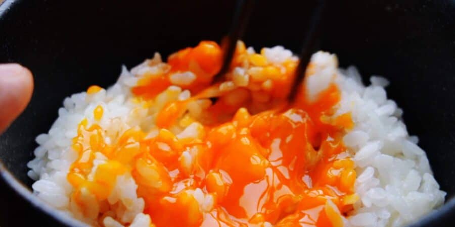 Breaking a raw egg yolk onto a bowl of Tamago Kake Gohan.