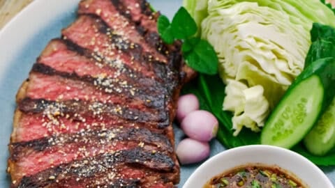 Crying Tiger Beef, highlighting the juicy texture of the meat with crunchy toasted rice and a bowl of vibrant Nam Jim Jaew sauce for dipping the steak.