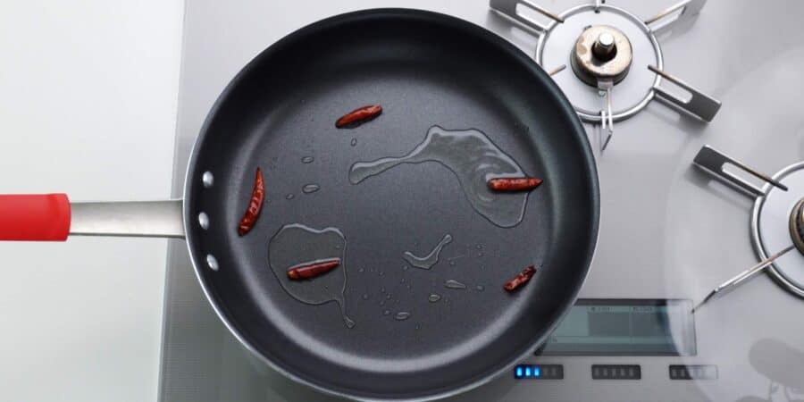 Frying red chili peppers in a large frying pan with oil.