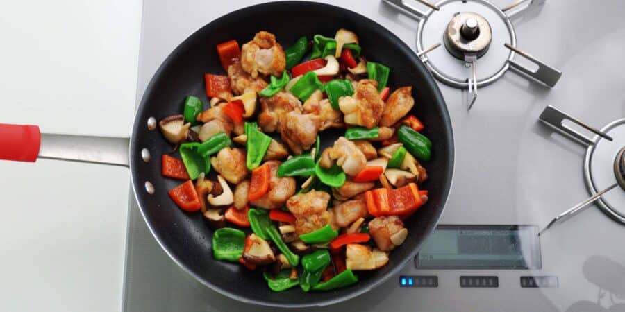 Hunan style chicken with chicken and red and green peppers in a pan.