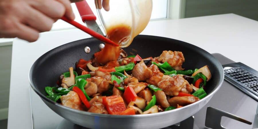 Adding Hunan chicken sauce to a frying pan of chicken and peppers.