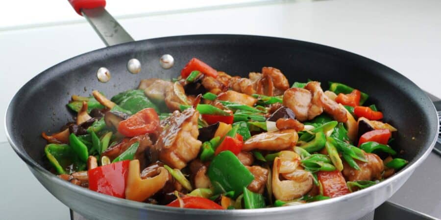 Hunan chicken in a frying pan with marinated chicken, mushrooms, peppers, and scallions.