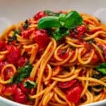 Side-view of a bowl of Pasta Pomodoro, showing the depth and layers of spaghetti intertwined with chunks of ripe tomatoes and basil leaves. - 6