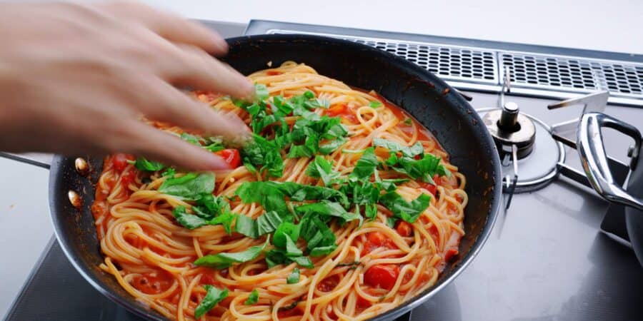 Sprinkling fresh basil on pasta pomodoro.