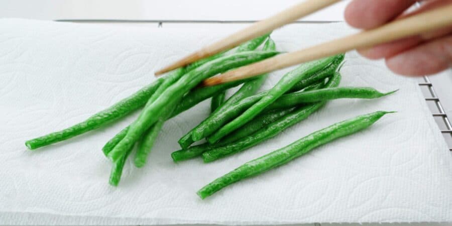 Flash fried green beans draining on a paper towel lined rack.