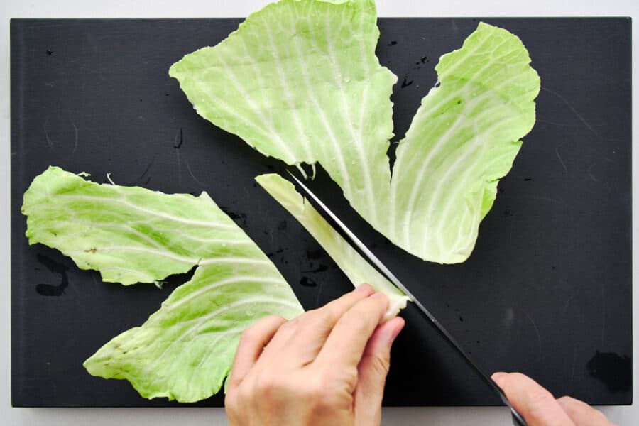 Cutting out the tough central stem from cabbage leaves with a knife.