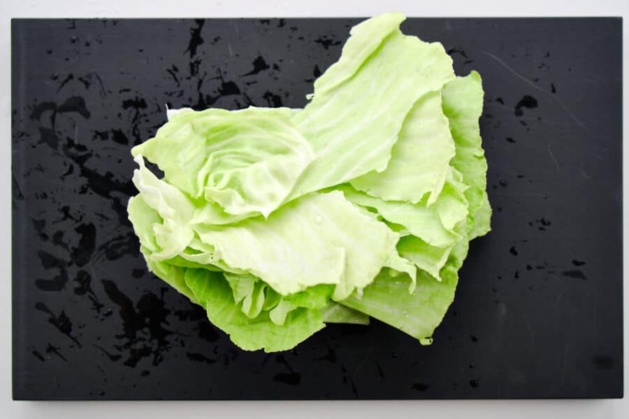 Stacking cabbage leaves up on a cutting board to shred.