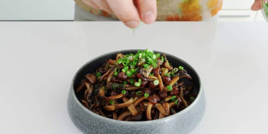 Garnishing a bowl of marinated mushrooms with scallions.