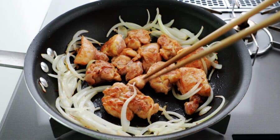 Flipping browned chicken over surrounded by onions.