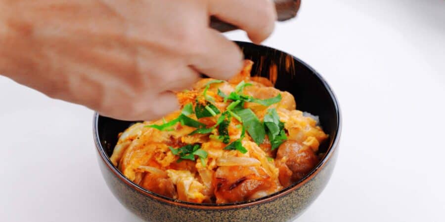 Shaking shichimi togarashi onto a bowl of oyakodon.
