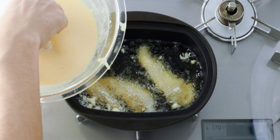 Adding tempura battered chicken strips to hot oil.