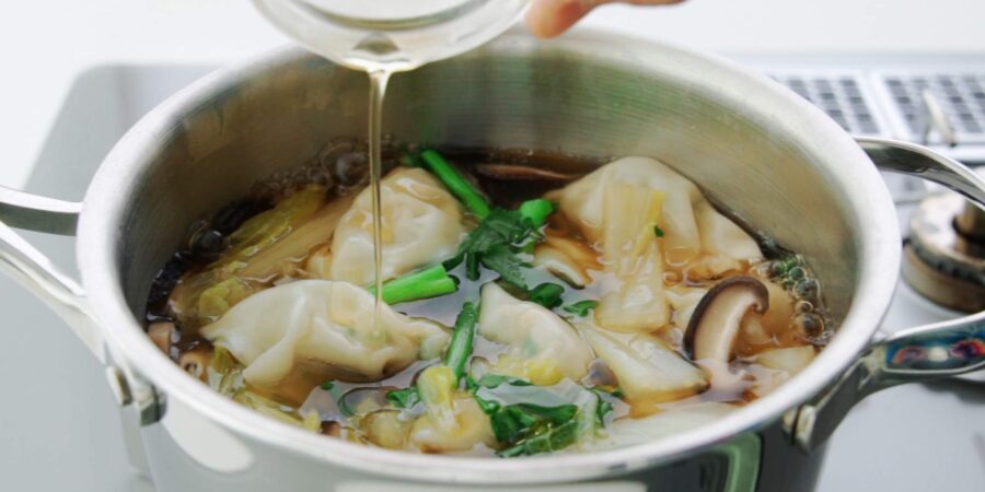 Adding toasted sesame oil to a pot of gyoza soup.